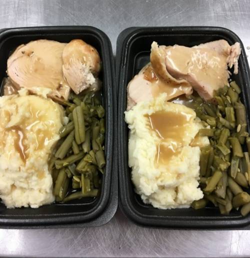 Two meal trays with sliced turkey in gravy, mashed potatoes, and green beans.