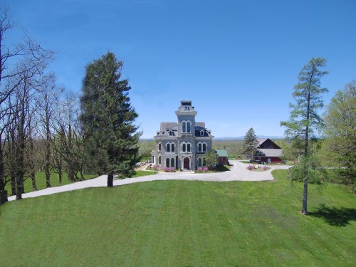 A large, ornate mansion surrounded by trees and a well-maintained lawn under a clear blue sky.