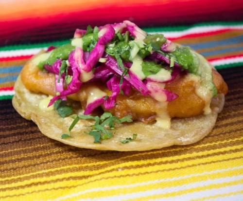 A colorful taco topped with green salsa, purple cabbage, and cilantro on a vibrant striped background.