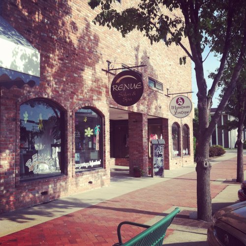 Exterior view of a brick building featuring Renue Salon & Spa and a nearby landscaping business, with trees lining the sidewalk.