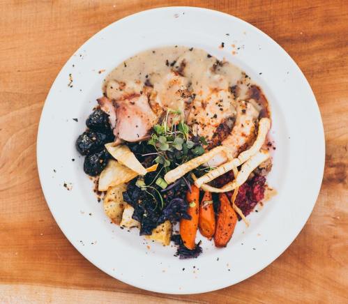 A plate of roasted vegetables, including carrots and parsnips, with sliced meat and a creamy sauce, garnished with herbs.