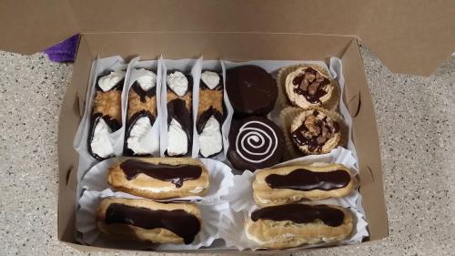 A box filled with assorted desserts: eclairs, cannoli, chocolate cupcakes, and cream-filled pastries.
