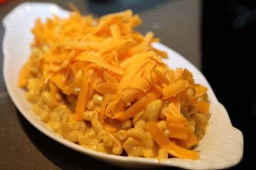 A serving of macaroni and cheese topped with shredded cheddar cheese on a white dish.