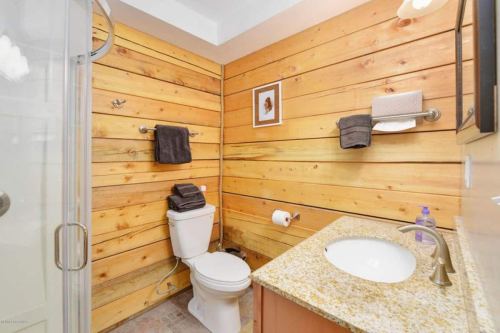 Cozy bathroom with wooden walls, a shower, toilet, and a granite sink with towels neatly arranged.