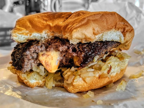Close-up of a juicy hamburger with melted cheese and sautéed onions on a soft bun, partially bitten.