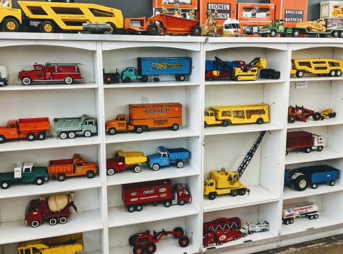 A display of vintage toy trucks and vehicles on white shelves, featuring various colors and designs.