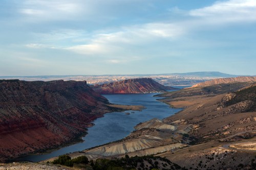 A scenic view of a winding river surrounded by rugged cliffs and rolling hills under a blue sky.