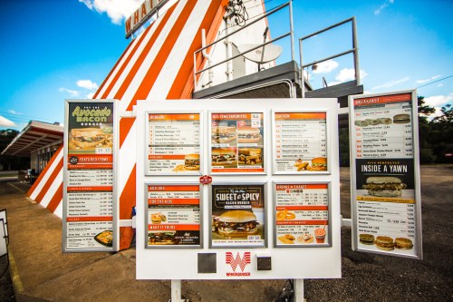 A colorful fast-food menu board featuring burgers, chicken, breakfast items, and prices at a drive-thru location.