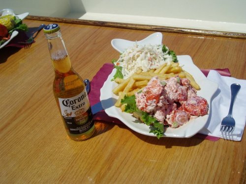 A plate of seafood salad with fries and coleslaw, accompanied by a bottle of Corona beer on a wooden table.