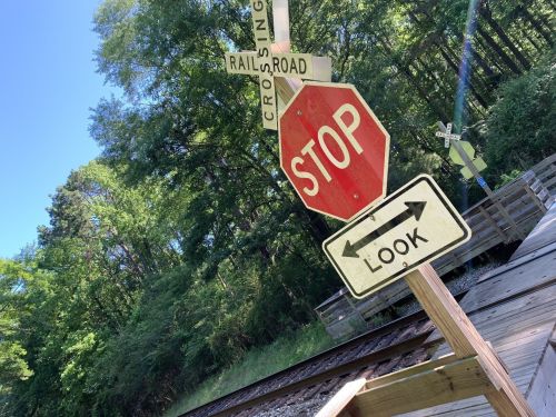 A stop sign and a look sign at a railroad crossing, surrounded by trees and a clear blue sky.