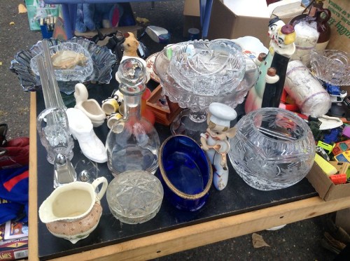 A table filled with various vintage glassware, ceramics, and collectibles at a flea market.