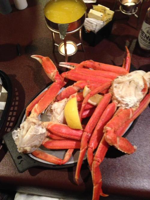 A platter of crab legs with lemon slices, served on a black tray, alongside a drink in the background.