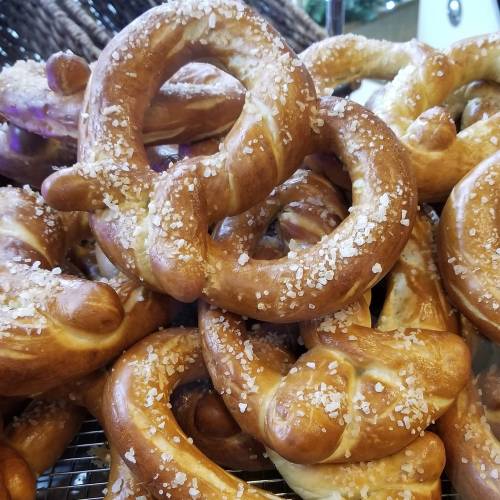 A close-up of freshly baked, golden-brown pretzels sprinkled with coarse salt, piled together.