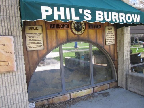 Entrance to "Phil's Burrow," featuring a green awning and informational signs about weather and groundhogs.