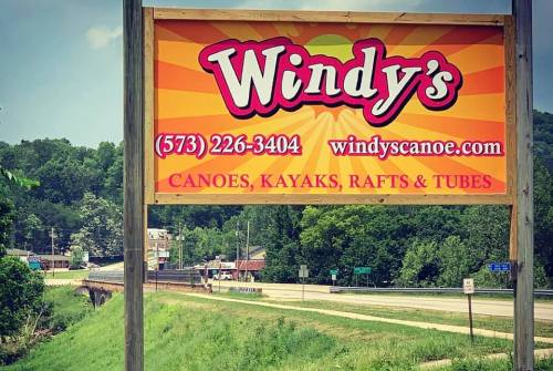 Sign for Windy's featuring contact info and services: canoes, kayaks, rafts, and tubes, set against a green landscape.