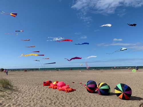 Colorful kites flying in the sky over a sandy beach, with vibrant beach balls scattered on the ground.