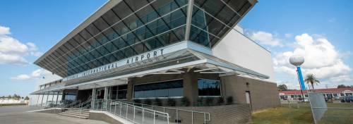 Exterior view of a modern airport terminal with large glass windows and a blue sky in the background.