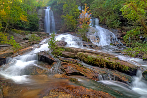 A serene waterfall cascades over rocky terrain, surrounded by lush green trees and autumn foliage.