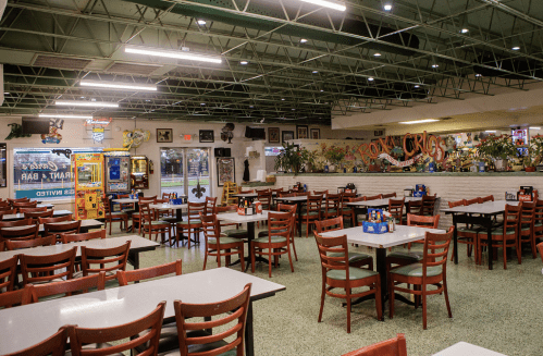 A spacious restaurant interior with empty tables, colorful decor, and a vibrant mural on the wall.