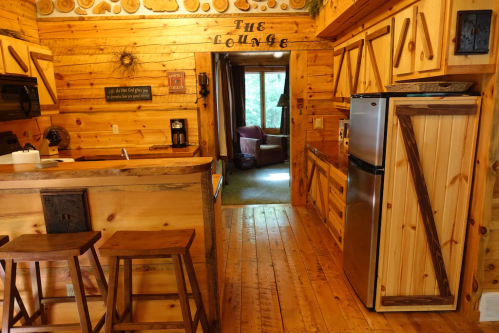 Cozy wooden cabin interior featuring a kitchen, lounge area, and natural light from a window.