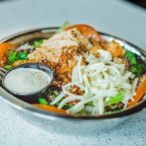 A colorful salad bowl with greens, tomatoes, crispy chicken, cheese, and a side of dressing.