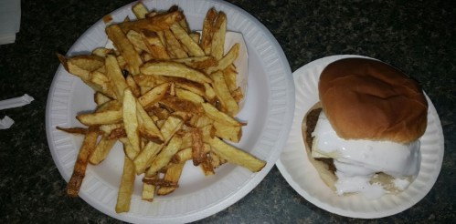 A plate of golden fries next to a burger topped with white sauce on a bun, served on paper plates.