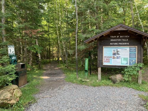 A nature preserve entrance with a sign, trail path, and surrounding trees in a lush green forest.