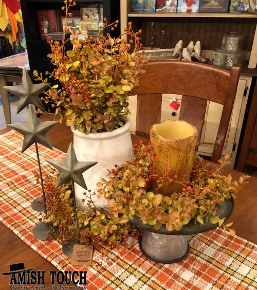 A rustic table setting with a white vase, candle, and decorative greenery, accented by star-shaped decor.