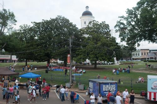 A festive outdoor scene with people gathered, food stalls, and a large building in the background, celebrating a holiday.