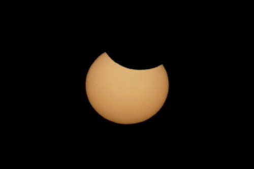 A partial solar eclipse with a crescent shape visible against a black sky.