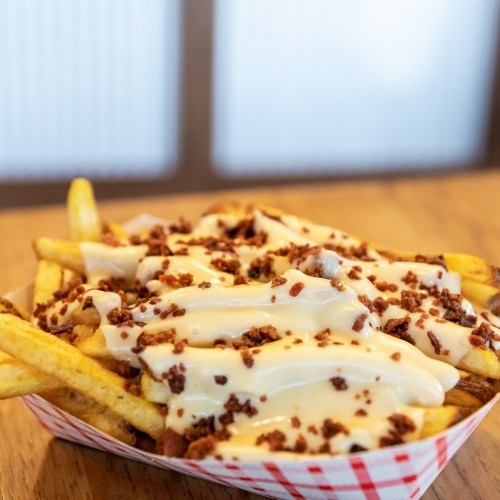 A serving of fries topped with creamy sauce and crumbled bacon, served in a red and white checkered tray.
