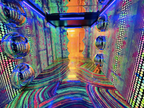 A vibrant, colorful room with reflective surfaces and swirling patterns, illuminated by neon lights.