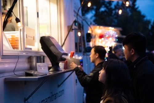 A food truck at night with customers ordering, illuminated by string lights and a warm glow from the truck.