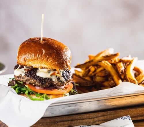 A juicy burger with lettuce, tomato, and sauce, served with a side of crispy fries on a metal tray.