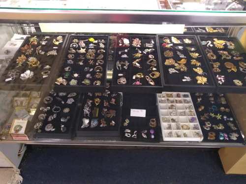 A display case filled with various brooches and pins arranged on black velvet trays.