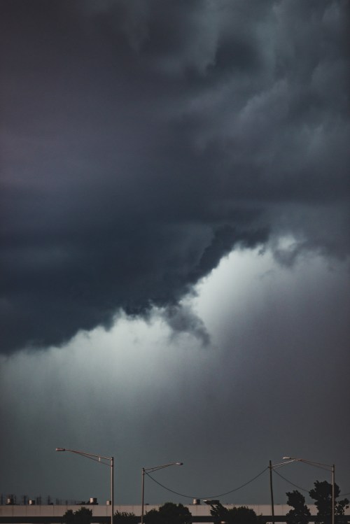 Dark storm clouds loom ominously over a cityscape, with hints of light breaking through the dense atmosphere.
