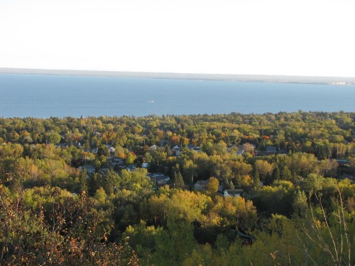 Aerial view of a lush green landscape with a lake in the background, showcasing autumn colors and a clear sky.