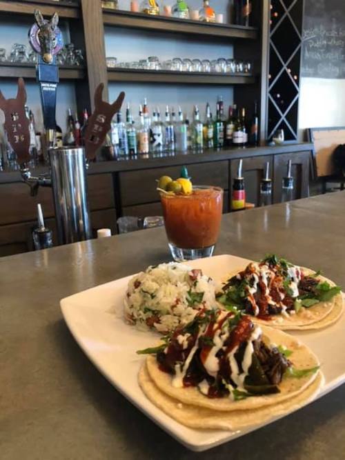 A plate of tacos with toppings and a side of rice, alongside a cocktail on a bar counter.