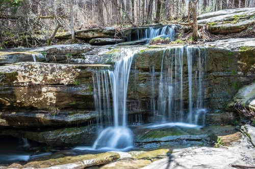 A serene waterfall cascades over moss-covered rocks in a lush forest setting.