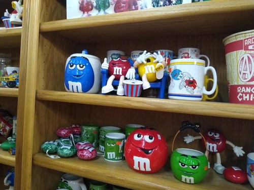 Colorful M&M's merchandise displayed on wooden shelves, including mugs and figurines in various designs.