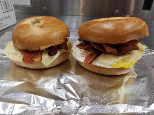 Two bagel sandwiches with bacon, cheese, and egg, placed on a silver foil surface.