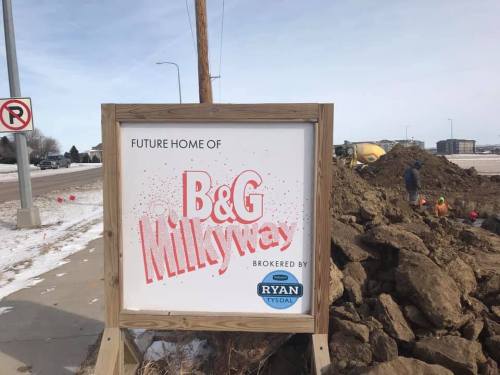 Sign announcing the future home of B&G Milkyway, with construction activity and a pile of dirt in the background.