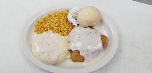 A plate of chicken fried steak with gravy, mashed potatoes, corn, and a roll, accompanied by a butter packet.