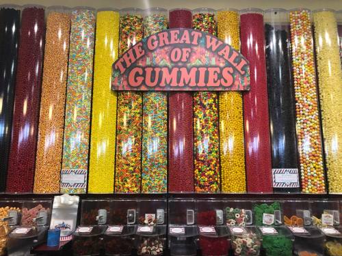A colorful display of various gummy candies in tall containers, labeled "The Great Wall of Gummies."