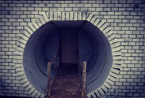 A large circular tunnel entrance with a brick exterior and wooden railing leading inside.