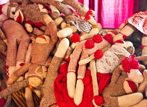 A colorful pile of handmade sock dolls in various outfits, featuring red accents and playful designs.