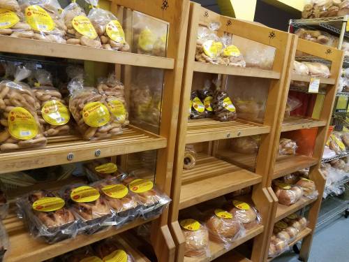 Shelves filled with various baked goods, all packaged and labeled, showcasing a variety of breads and cookies.
