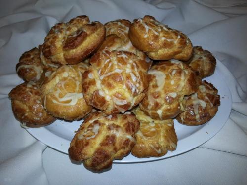 A plate of freshly baked pastries drizzled with icing, arranged on a white cloth.