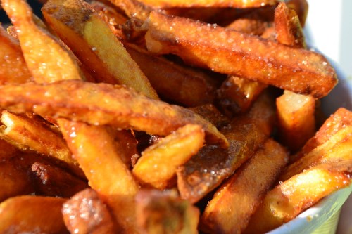 A close-up of golden, crispy French fries piled in a bowl, glistening with oil and sprinkled with salt.