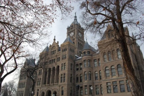 Historic building with a clock tower, surrounded by bare trees and a cloudy sky.